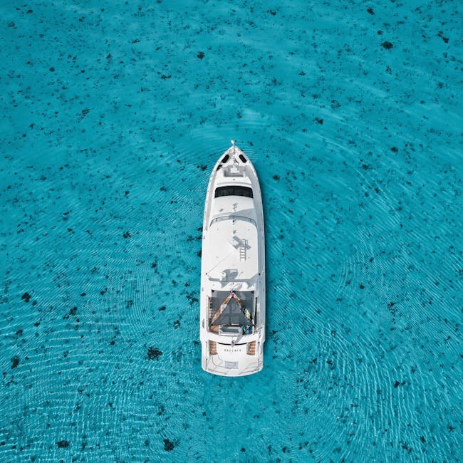 Top-down view of a white yacht in clear turquoise waters, surrounded by ripples.